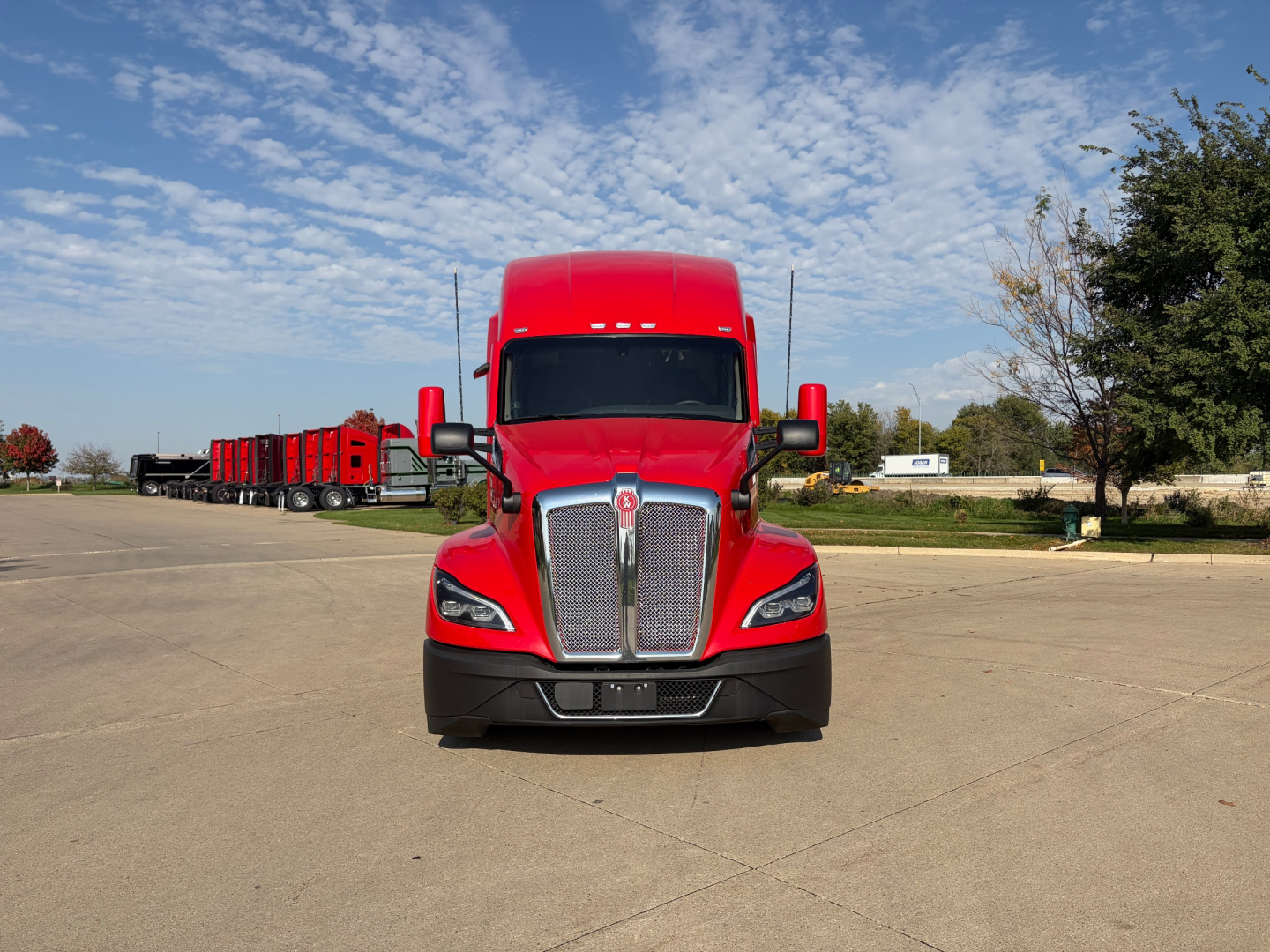Kenworth T680 front view in red with large grille and hood, truck in a parking lot.