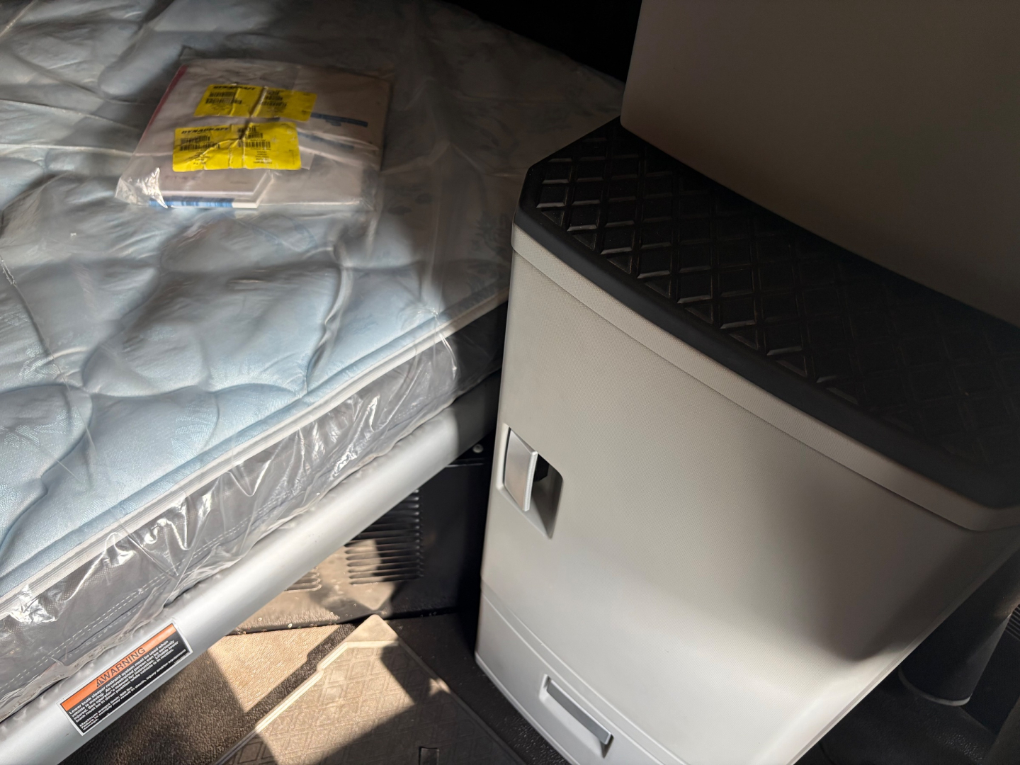Kenworth T680 cab interior showing storage area and folded sleeper with stickered packaging on mattress edge.