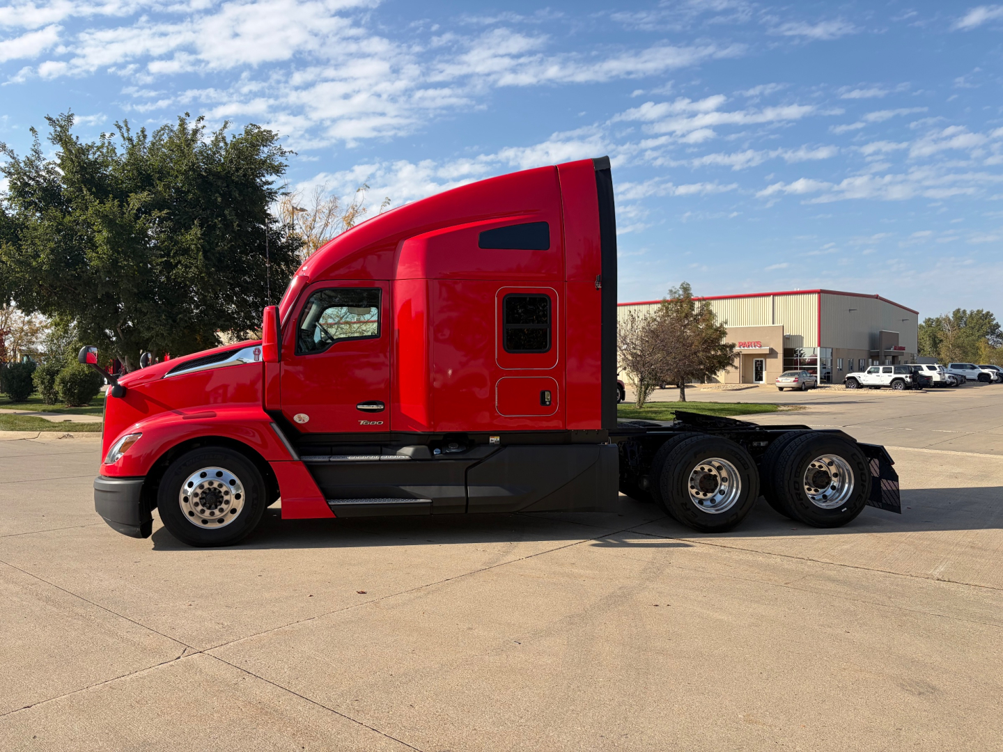 Kenworth T680 tractor in red, side view showing sleeper cab, rear tandem wheels, and chassis.