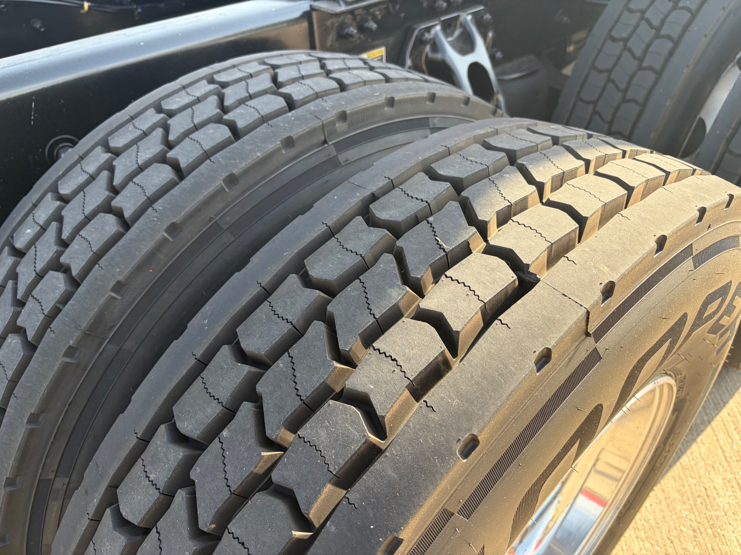 Kenworth T680 wheel and dual rear tires seen in close-up with tread pattern and rim; part of truck chassis visible.