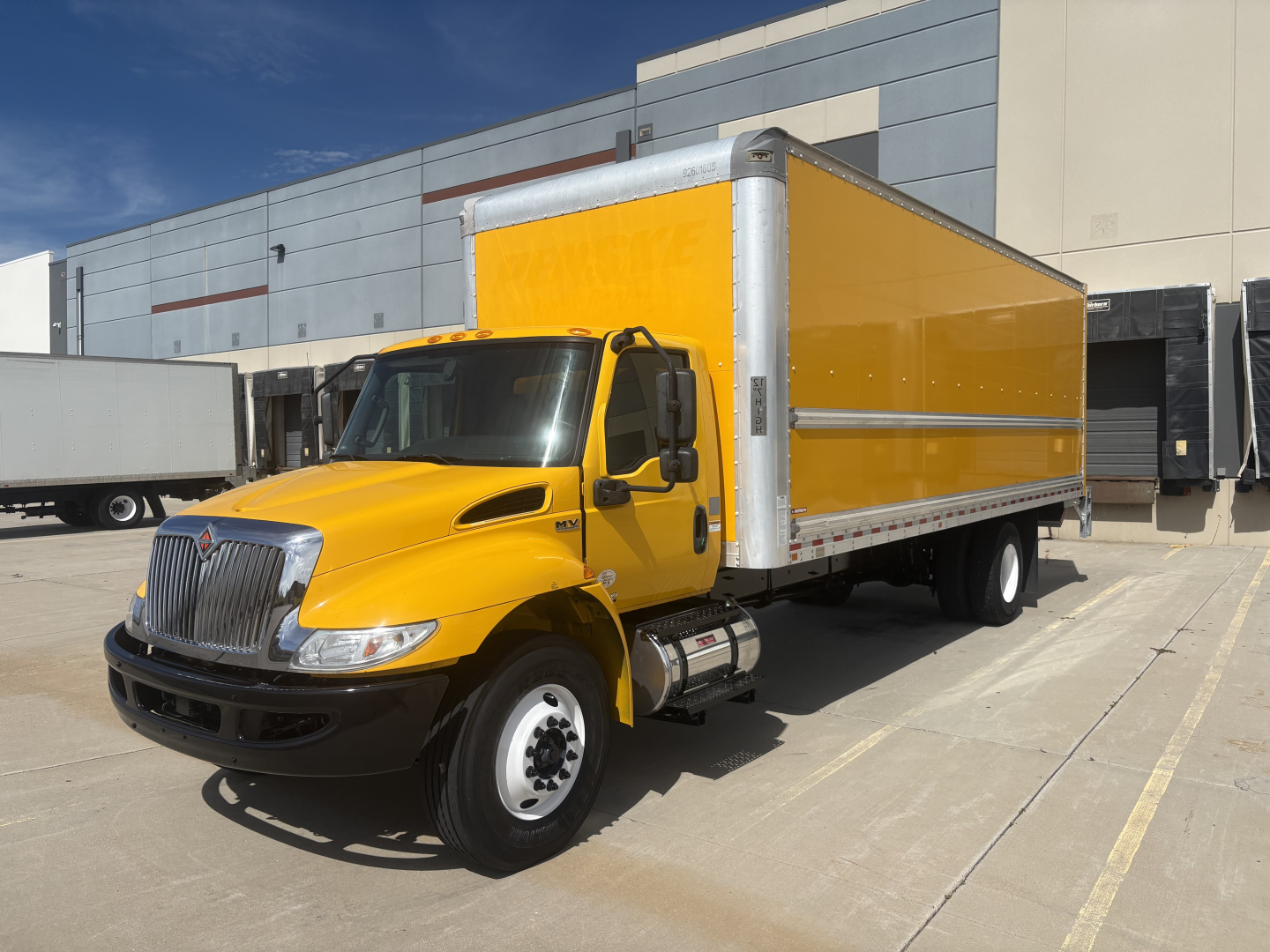 Box truck with bright yellow cargo body and cab, International MV Series, parked in lot with industrial building.