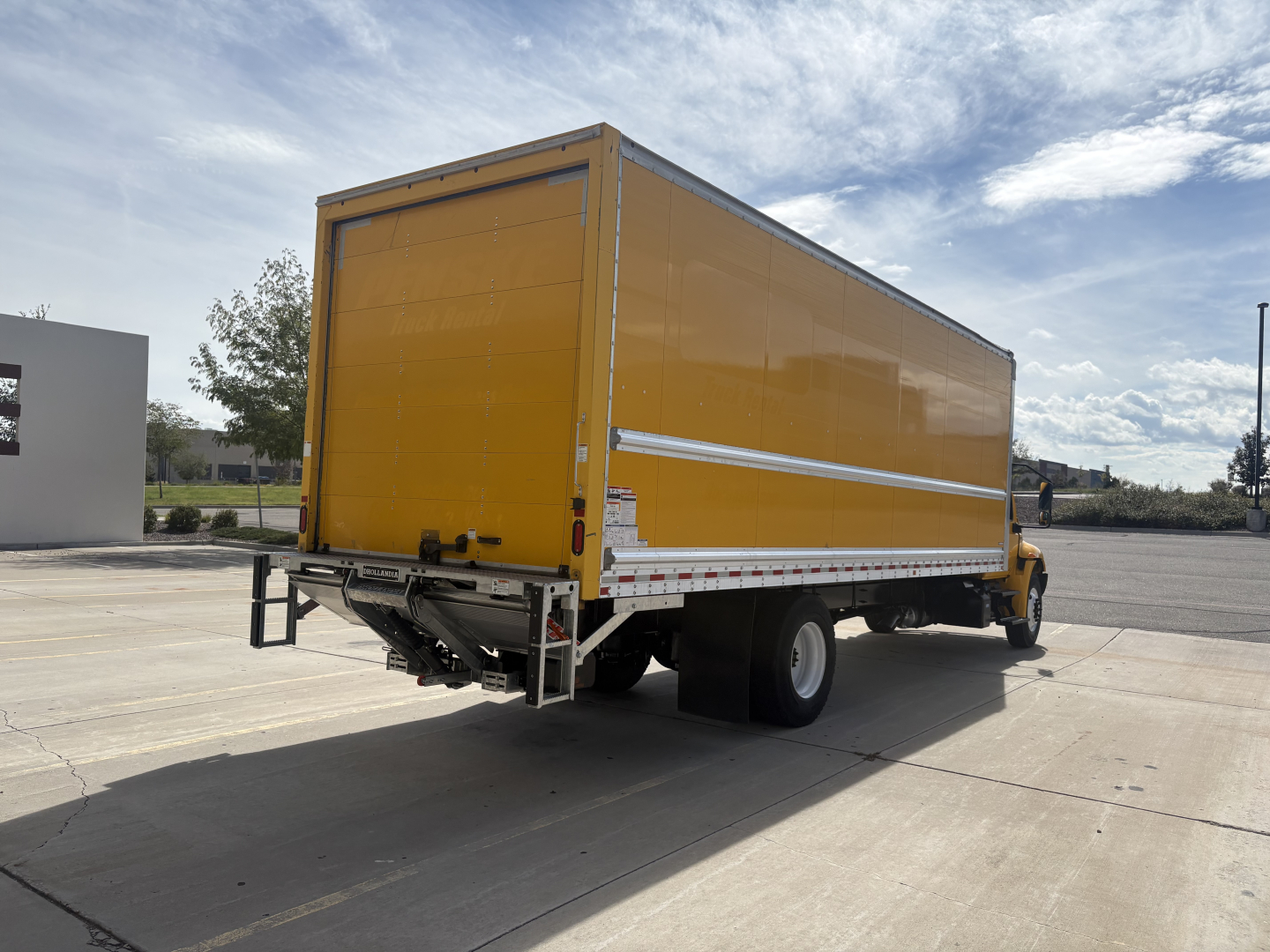 Box truck in yard showing bright yellow cargo box and cab, International MV chassis with rear swing doors and black tires.