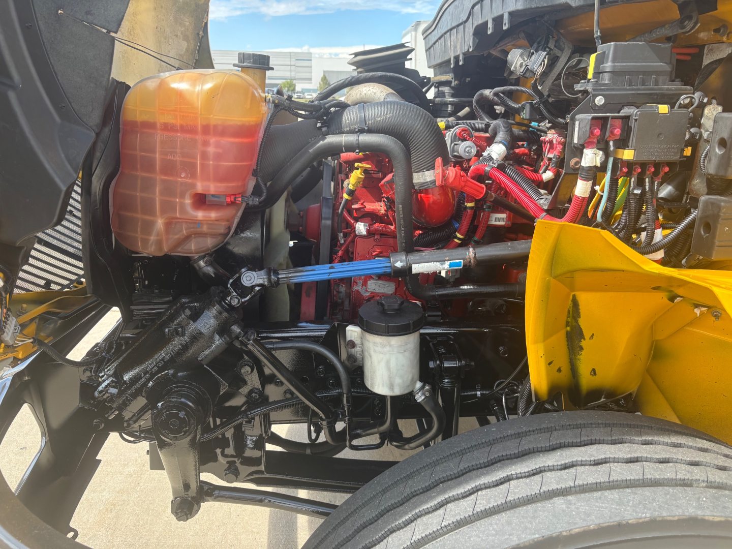 Truck engine bay showing coolant reservoir, various hoses, and engine components in red and black with a yellow body part visible.