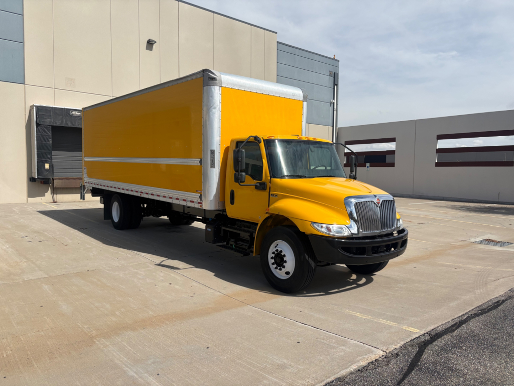 Box truck with yellow cargo body and cab, International logo, in-service vehicle on concrete lot.