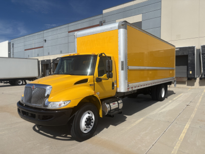 Box truck with bright yellow cargo body and cab, International MV Series, parked in lot with industrial building.
