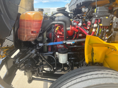 Truck engine bay showing coolant reservoir, various hoses, and engine components in red and black with a yellow body part visible.