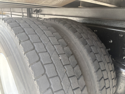 Trailer wheel and dual rear tires under truck frame showing tread blocks and tire sidewall.