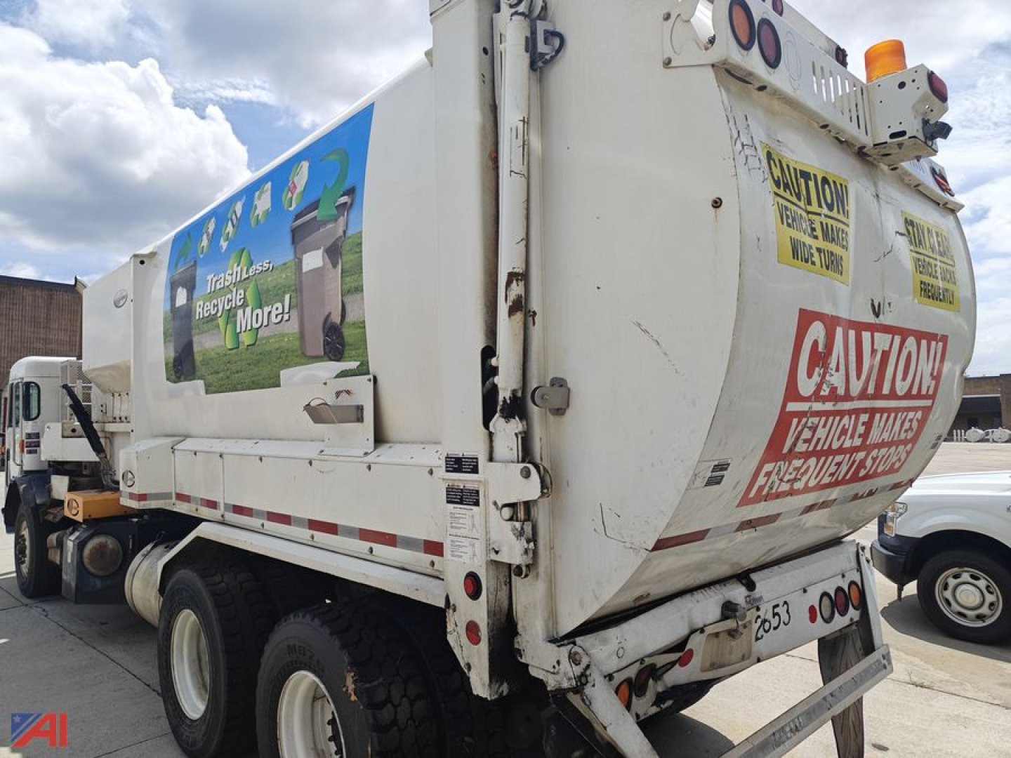 Peterbilt 320 garbage truck rear and side view showing large rear compactor and caution signage.