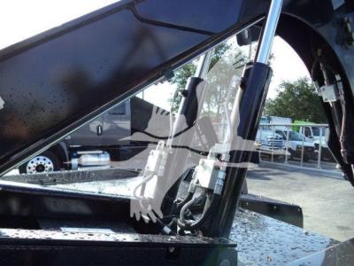 Ram 5500 Big Horn winch truck showing hydraulic shock strut and winch components under an open hood with surrounding vehicles in background.