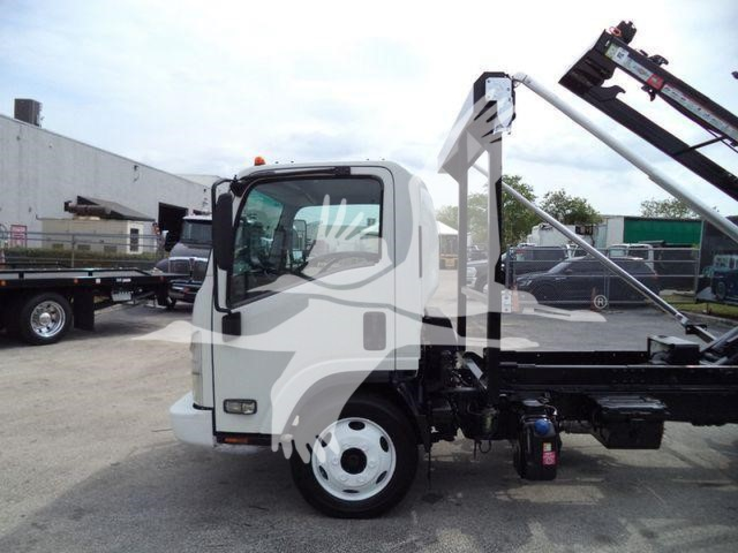Isuzu NPR/NRR medium-duty cab-forward truck with roll-off hoist, side view showing white cab, black chassis, and hydraulic arm under bright sky.
