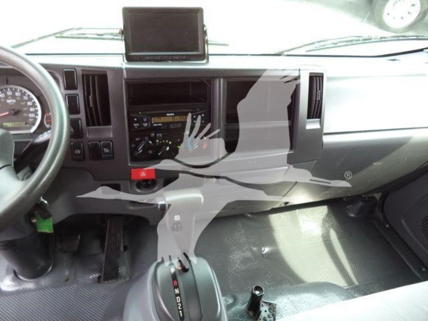 Isuzu NPR/NRR cabin dashboard view showing steering wheel left, center console, gear shifter, and a tablet mount on dash.