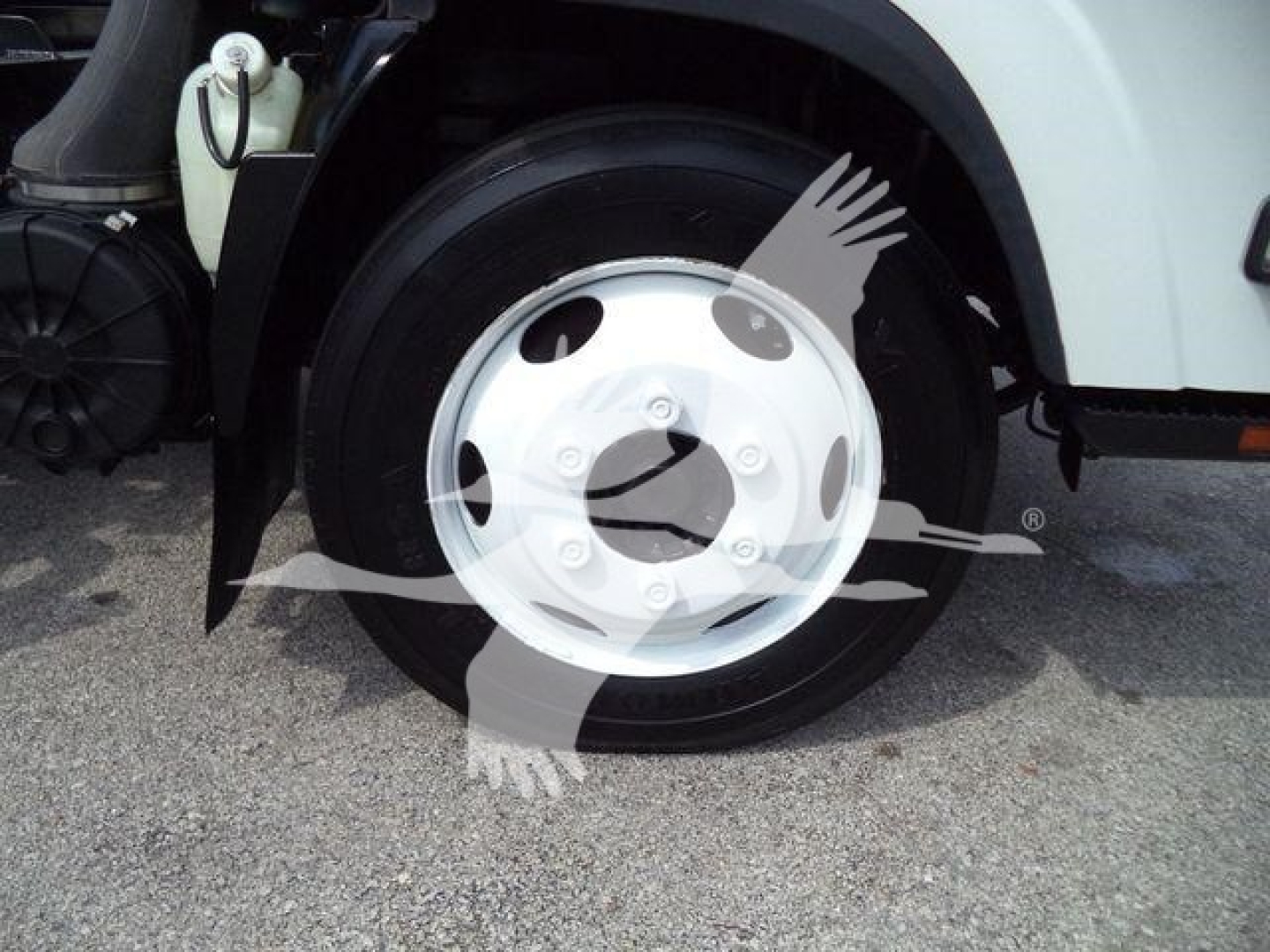 Front wheel and tire of a 2017 Isuzu NPRR roll-off truck showing wheel, hubcap, and part of front fender.