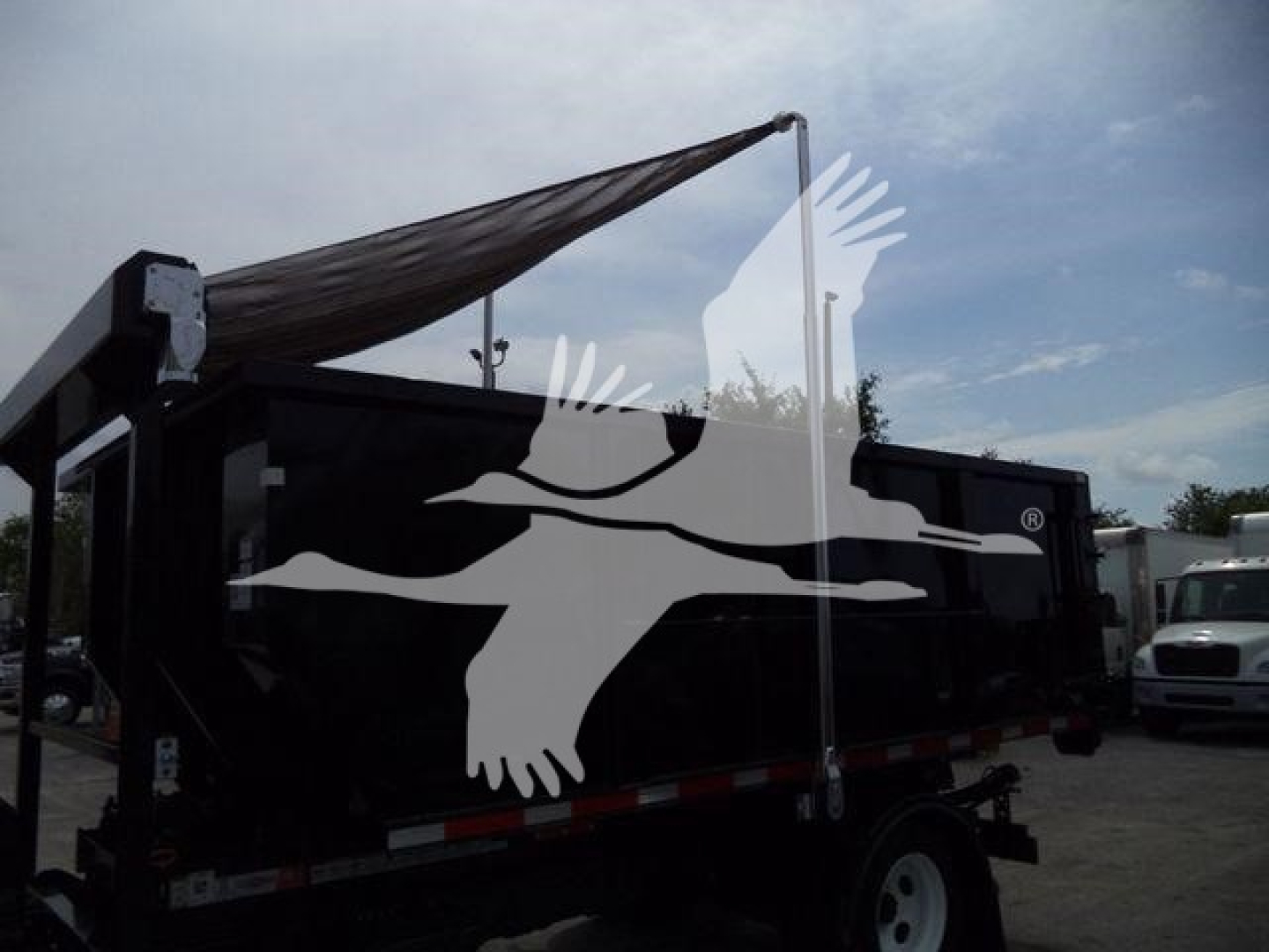 Isuzu roll-off truck bed with black paint, side panels, white wheel, and a white graphic of a bird in flight overlaying. Visible text on labels not legible.