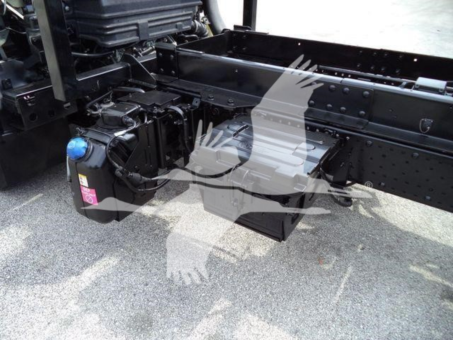 Isuzu NPR (Nrr) truck chassis view showing fuel/wiper reservoir, frame rails, and battery box. Visible components include a black battery tray and blue cap of a fluid reservoir.