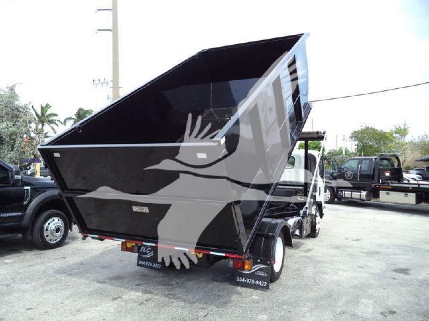 Isuzu NRR truck with a raised black dump bed in a lot; rear view shows license plate area and small text on mudflaps; no other readable labels visible.
