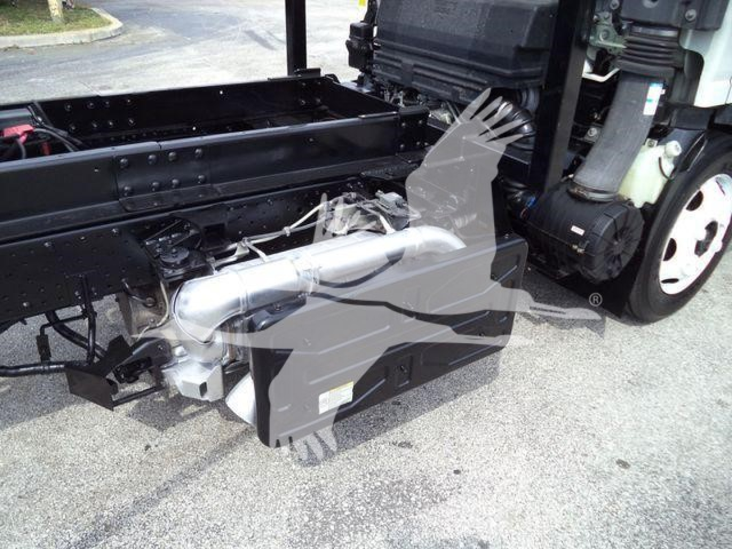 Isuzu NPR/NRR truck chassis showing a hydraulic system component and frame; side view with white cab wheel visible.