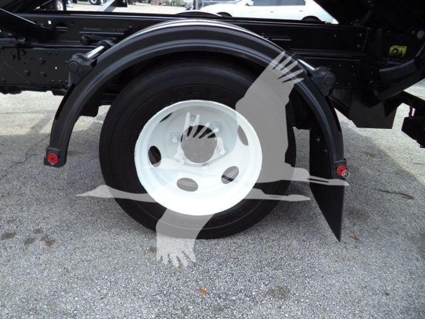 Isuzu NPRR/flatbed rear wheel and fender showing white steel wheel, black tire, and wheel arch; part of roll-off truck chassis.