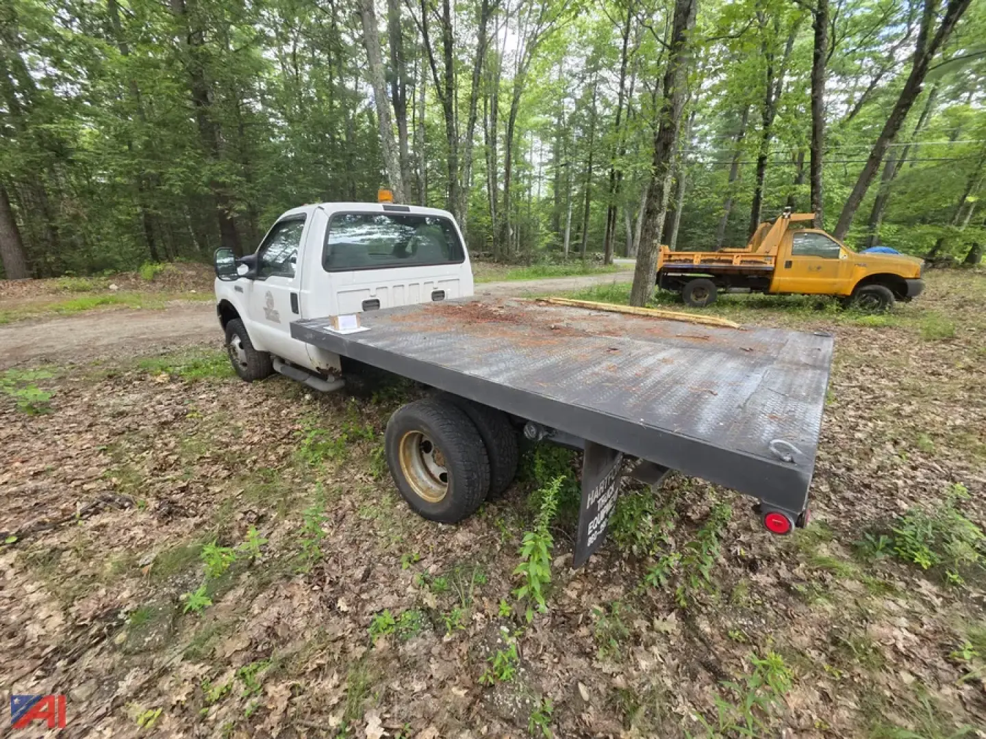 Ford F-350 Super Duty flatbed truck with long steel flatbed, white cab, in-service wooded area.