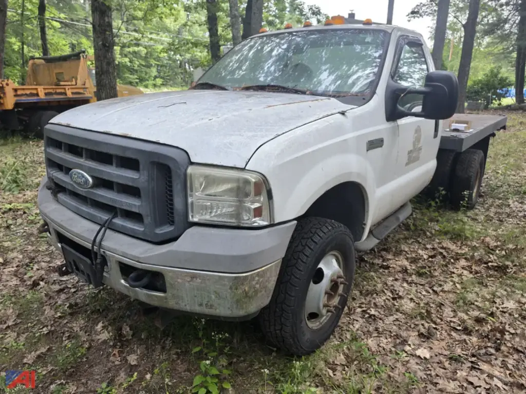 Ford F-350 Super Duty flatbed truck in a yard, front driver's side view, white with dirt and wear, flatbed rear, headlights and grille visible.