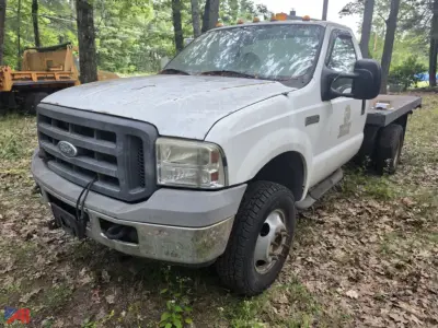 Ford F-350 Super Duty flatbed truck in a yard, front driver's side view, white with dirt and wear, flatbed rear, headlights and grille visible.