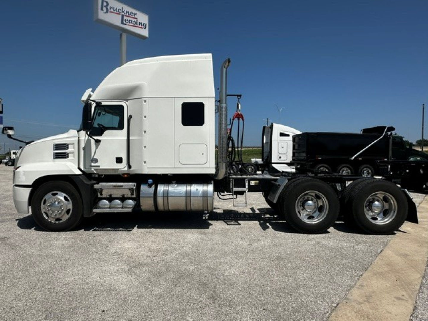 Truck side view 2020 Mack ANTHEM convention sleeper with chrome fuel tanks and dual rear axles in a dealership lot.