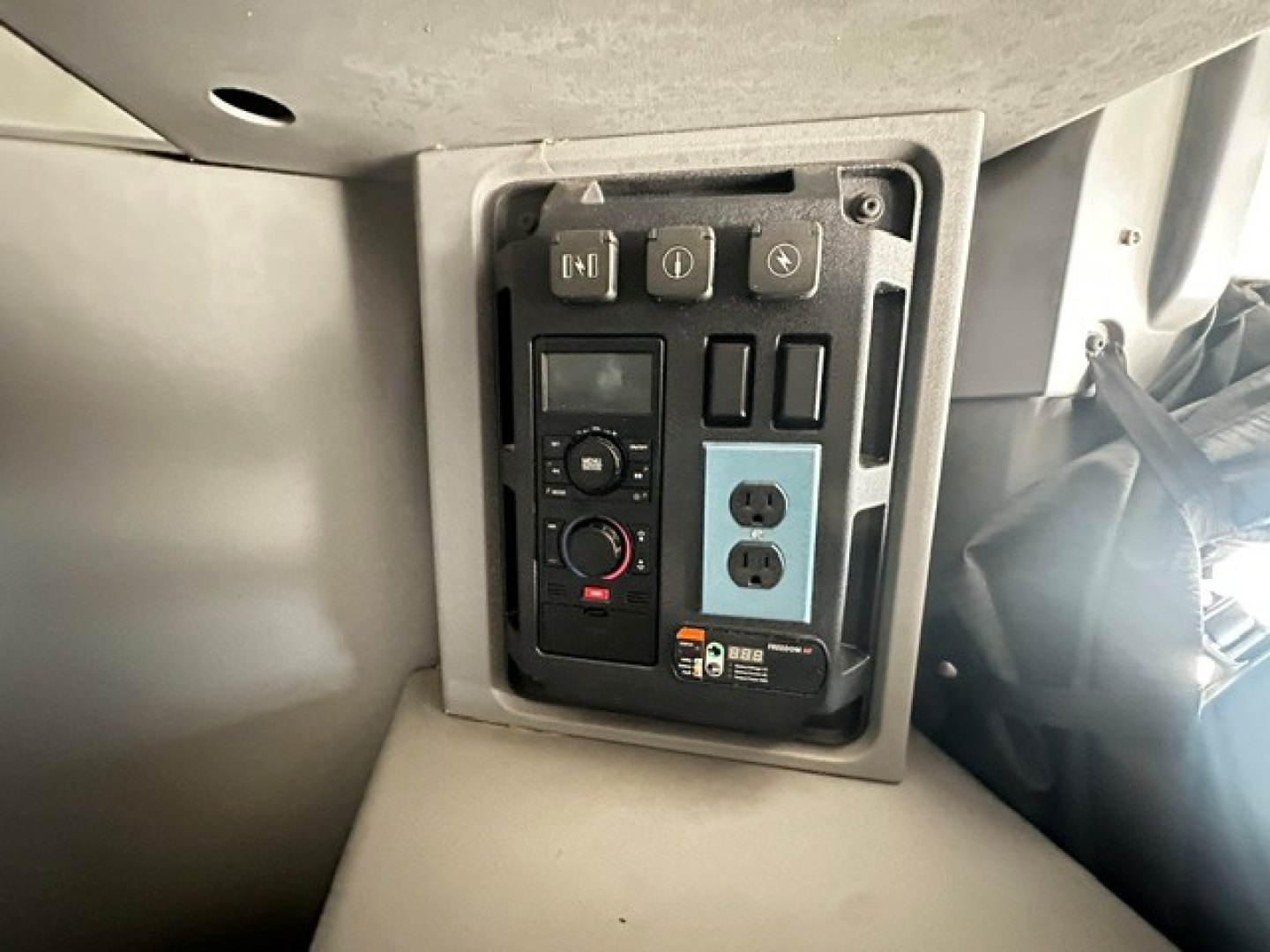 Cab control panel and power outlet panel inside a Mack ANTHEM, showing a two-outlet blue panel, various switches, circular dial, and warning labels.