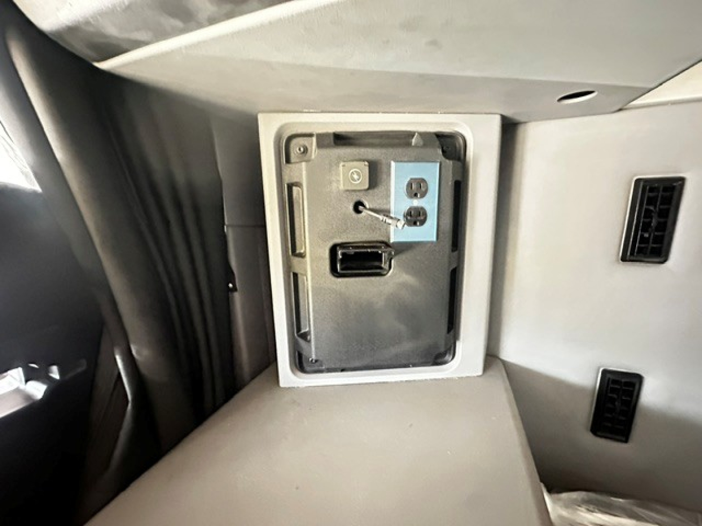 Vehicle cabin USB-C/HDMI-style port panel in dashboard area with a small metal plate and connector, surrounded by light grey interior panels.