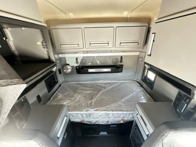 Truck cab bunk area of a 2020 Mack Anthem showing overhead storage, shelves, a mounted device, and a covered mattress.