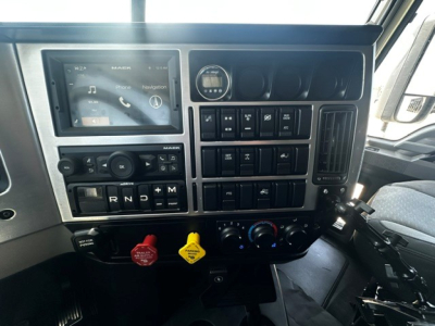 Dashboard of a Mack truck cab showing multiple controls, touchscreen display, steering wheel not visible, center console with buttons and knobs, red and yellow knobs, blue climate controls.