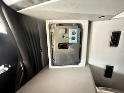 Vehicle cabin USB-C/HDMI-style port panel in dashboard area with a small metal plate and connector, surrounded by light grey interior panels.