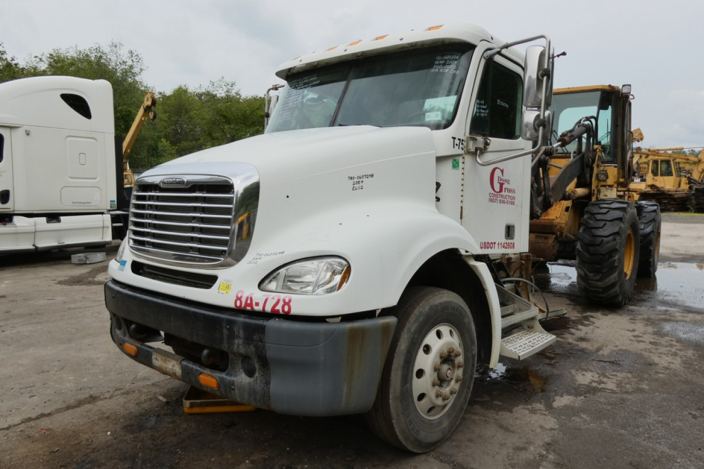 Truck cab and front end of a white 2006 Freightliner CL112 conventional daycab showing front grille, bumper, and side steps.