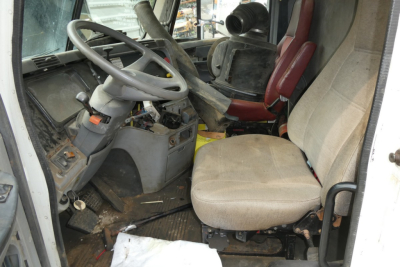 Cab interior of a Freightliner CL112 truck showing steering wheel, driver's seat, and dirty floor with worn controls.