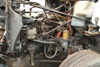 Truck engine bay of a 2006 Freightliner CL112 with visible hoses, wires, and reservoirs; includes coolant reservoir and power steering components.