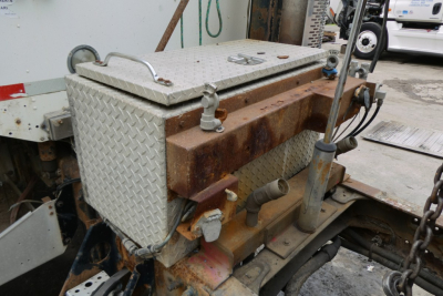 Truck equipment showing a diamond plate toolbox mounted on a rusted engine bay area with hydraulic controls and cables.