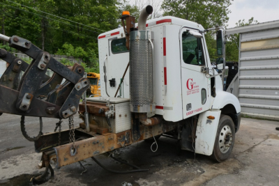 Truck rear-three-quarter view showing construction crane and exhaust stack with white cab and rusted rear frame.