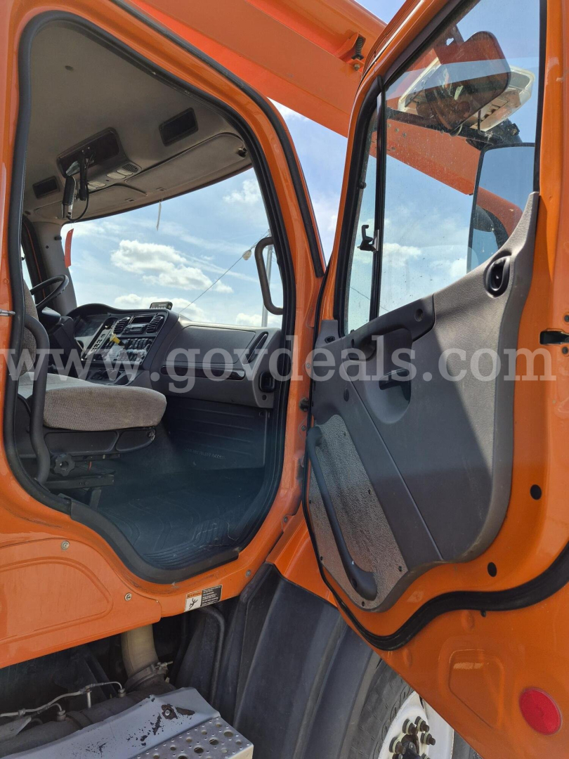 Freightliner cab interior with orange exterior showing dashboard and open door.