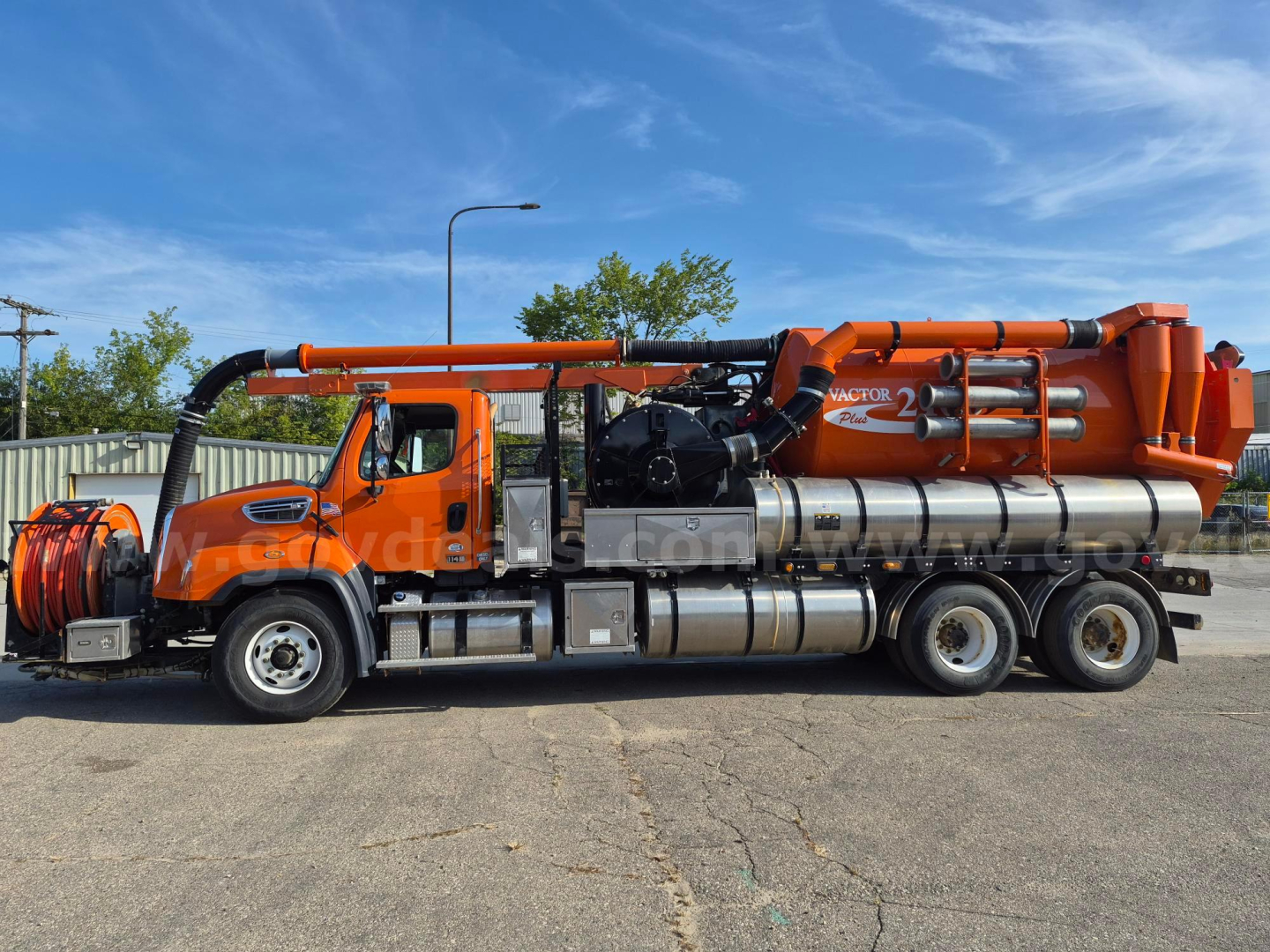 Freightliner 114SD vacuum truck with orange piping and stainless cylindrical tanks, side view.