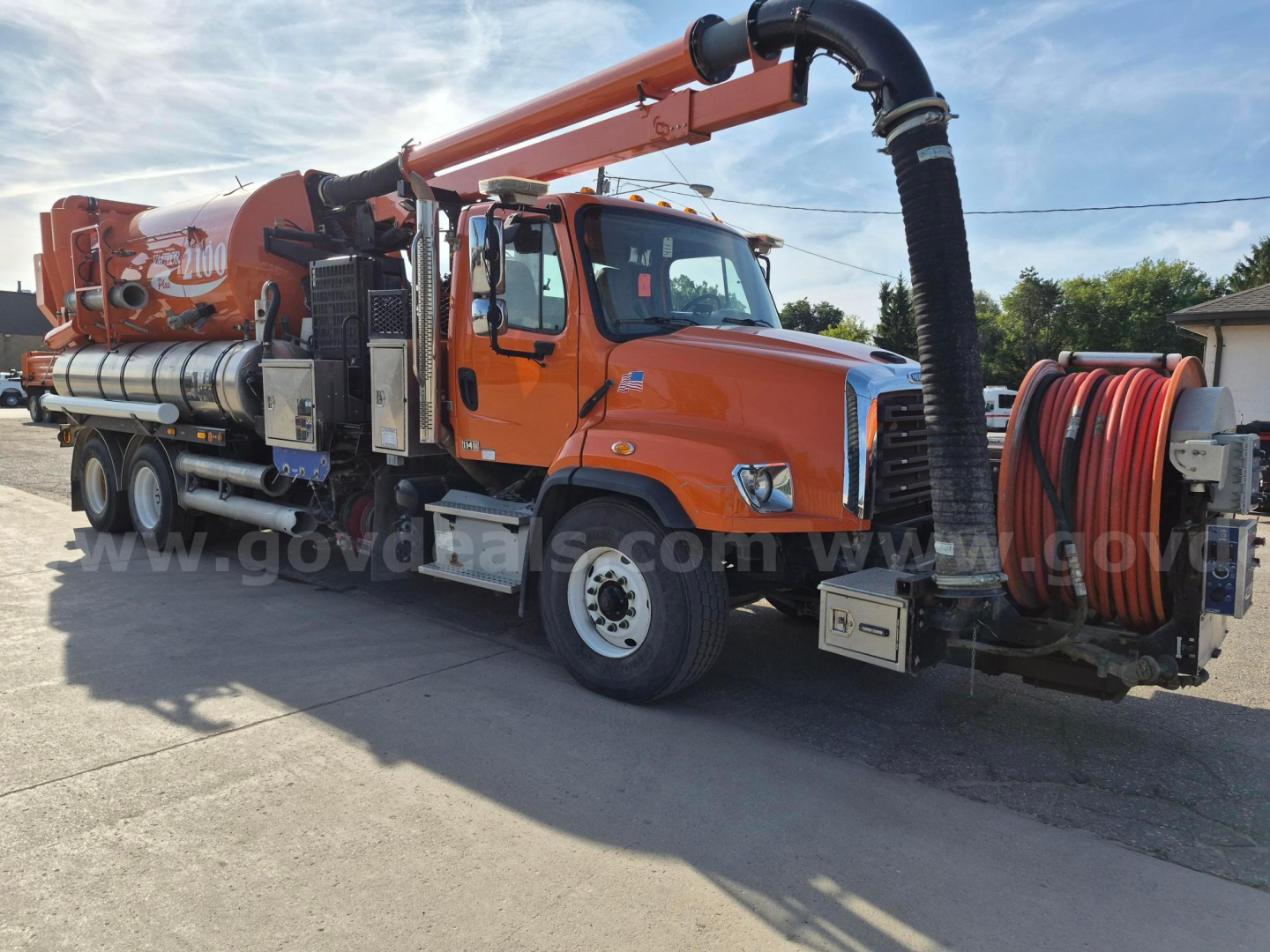 Orange Freightliner vacuum truck with hose reel and rear-mounted vacuum system, side text '3000' on tank, various equipment racks and hoses visible.