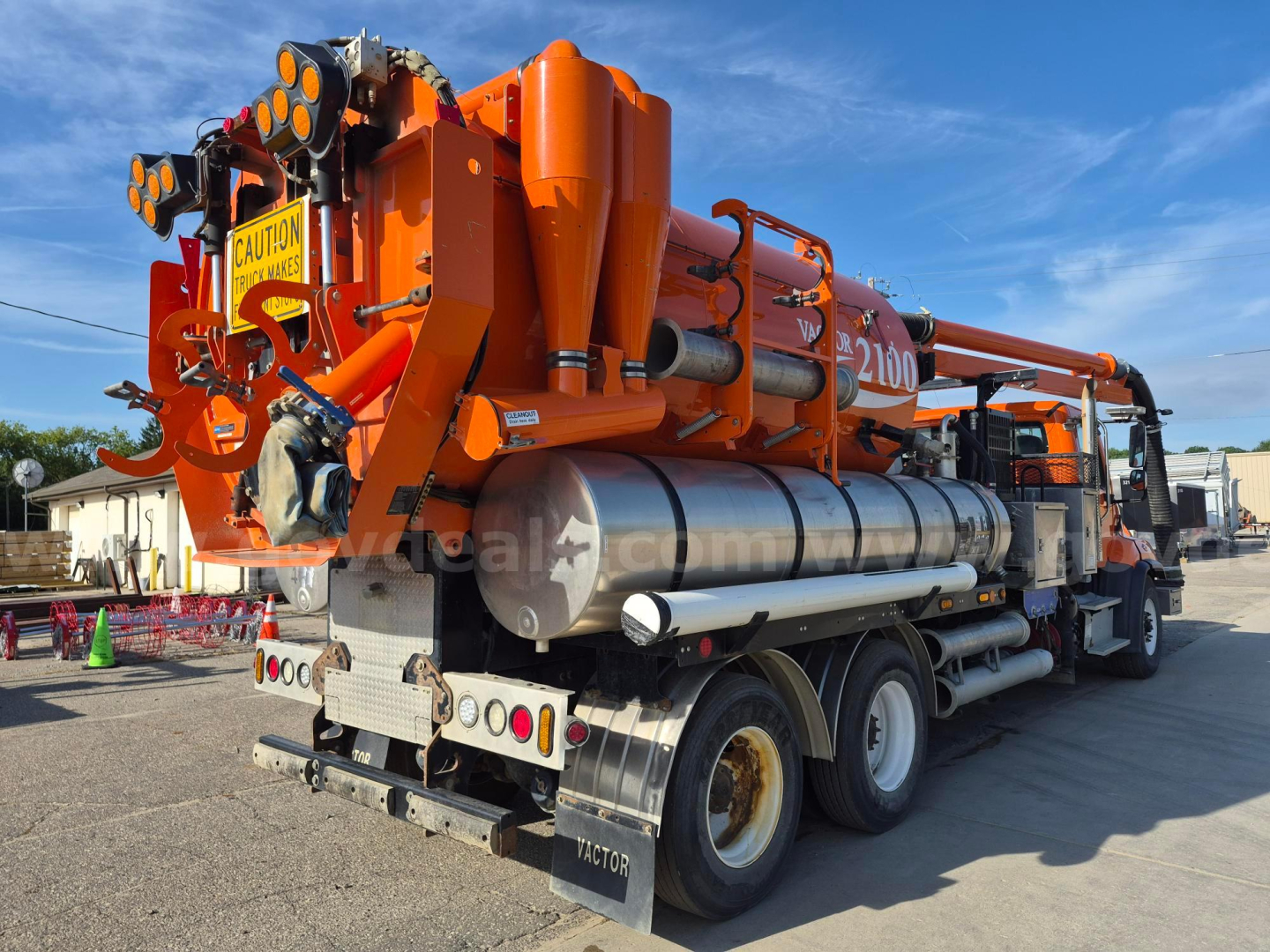 Freightliner 114SD vacuum truck rear and side view showing large orange vacuum system with tanks and hoses, dual rear axles, and warning decals.