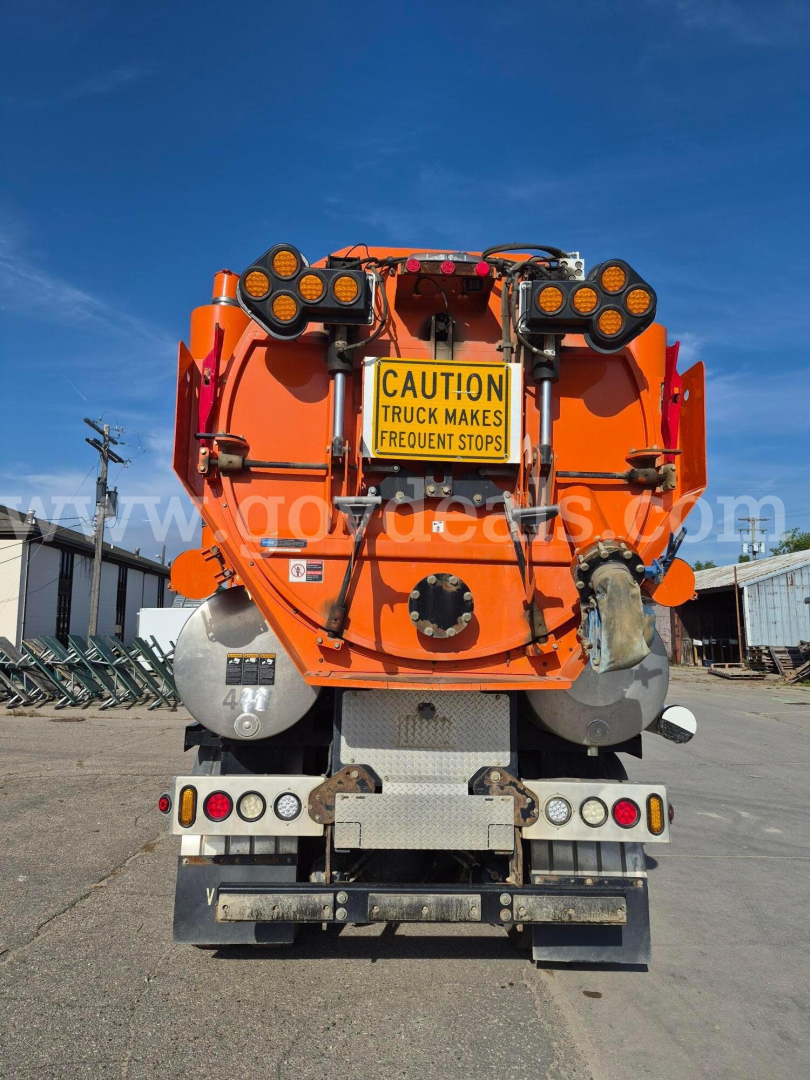 Rear view of a bright orange Freightliner vacuum truck showing warning sign, hoses, and dual rear wheels.