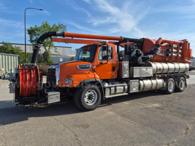 Orange Freightliner vacuum truck with long orange hose reel and multiple silver tanks.