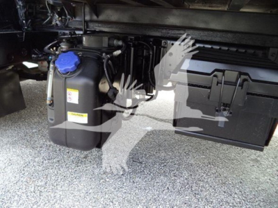 Isuzu NPR HD truck chassis showing coolant reservoir with blue cap and attached toolbox on the side.