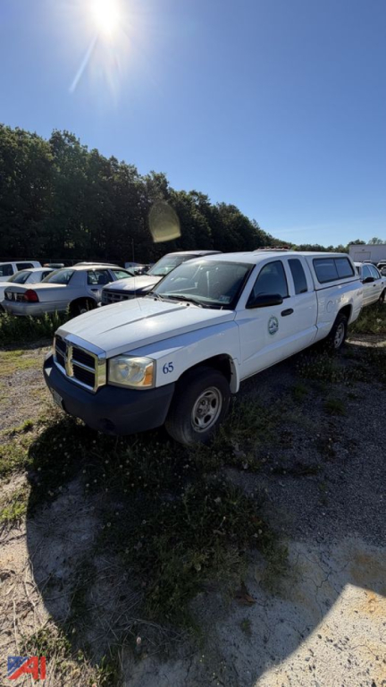 Dodge Dakota pickup truck with cap and white body in an outdoor lot; multiple vehicles in background; front-left view.