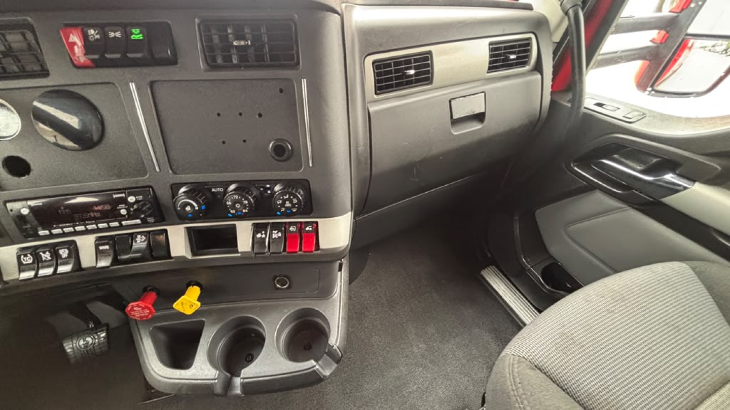 Kenworth T680 cab interior dashboard and steering wheel area with controls and storage compartments.