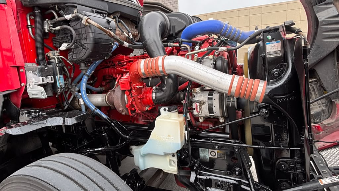 Kenworth T680 engine bay showing turbocharger, intercooler piping, coolant reservoir, and hoses with red engine block and blue silicone hoses.