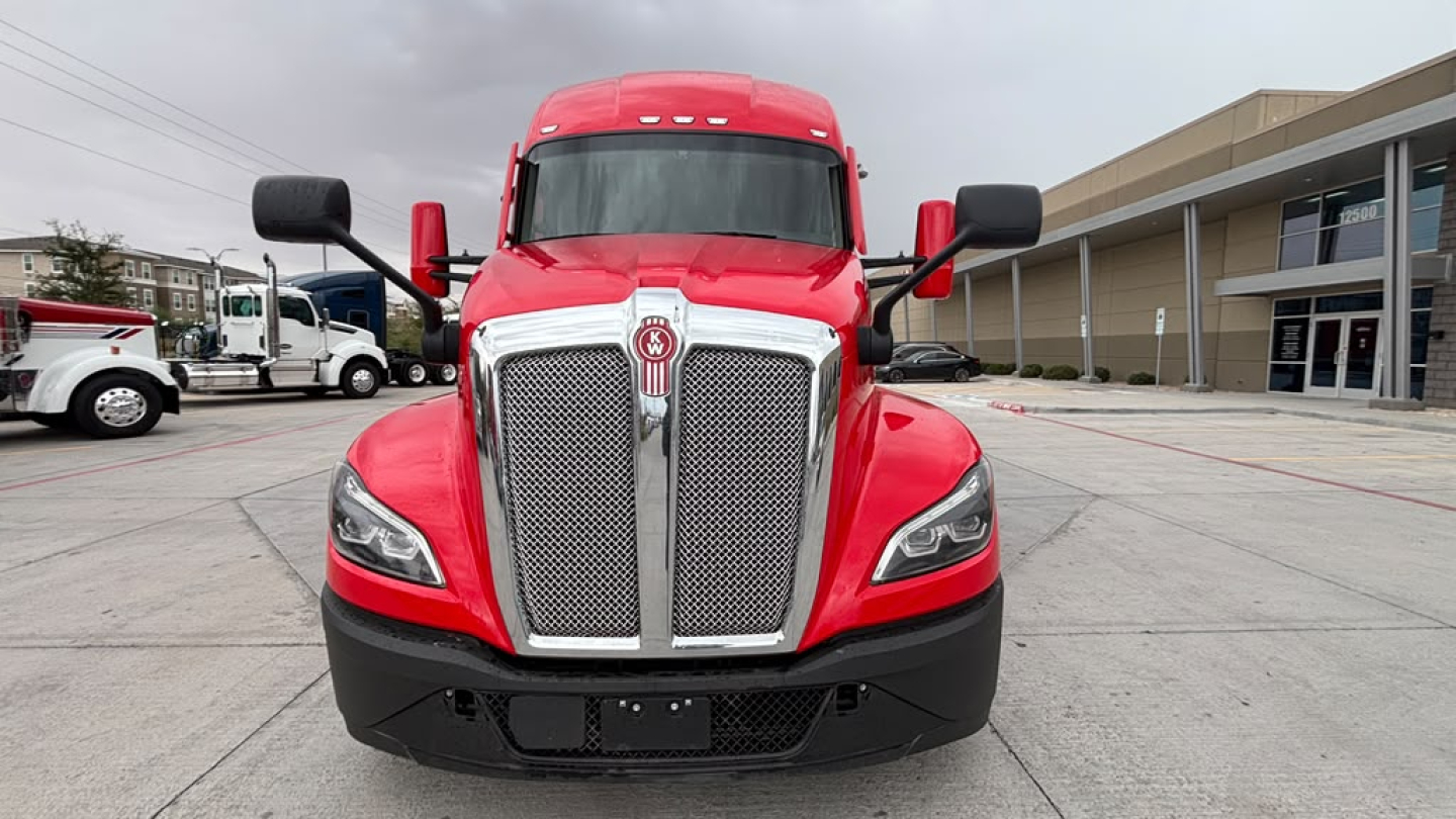Kenworth T680 truck front view showing bold chrome grille, red exterior, and black bumper.