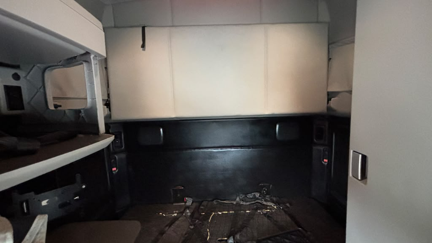 Kenworth T680 sleeper cab interior cargo area showing clean walls and floor with some tools and paneling.