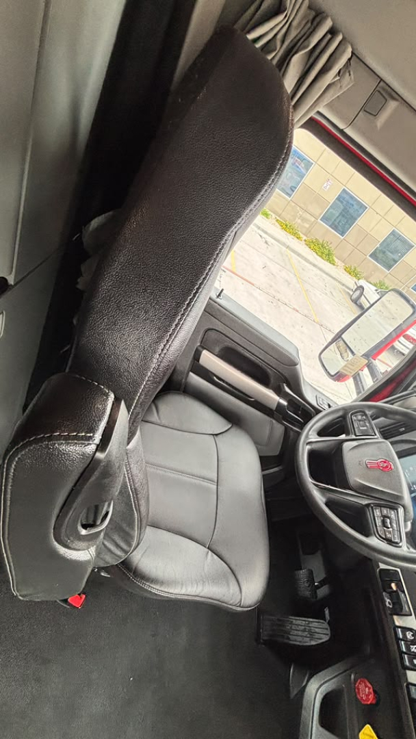 Cab interior of a 2023 Kenworth T680 showing driver seat, steering wheel with red Kenworth emblem, and dashboard controls.