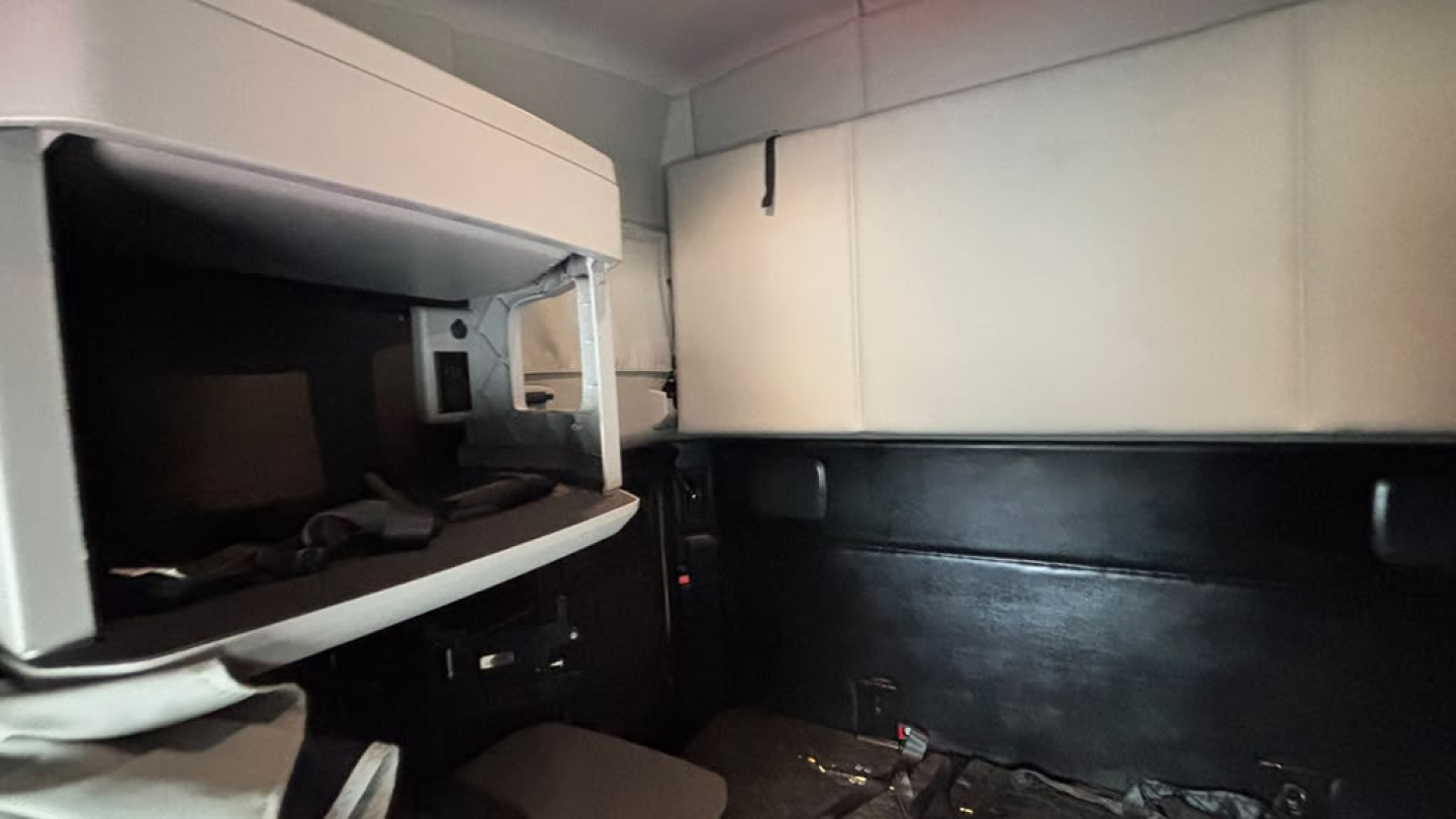 Interior of a Kenworth T680 cab showing dashboard storage shelf and sleeper area.