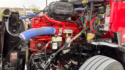 Kenworth T680 engine bay showing high-flow air intake and red engine with blue radiator hose, stickers and hoses visible.